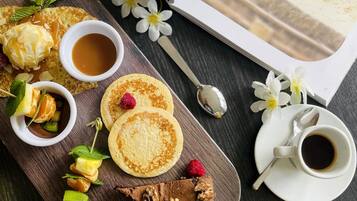 Un desayuno servido sobre una tabla de madera con panqueques, fruta y bebidas.