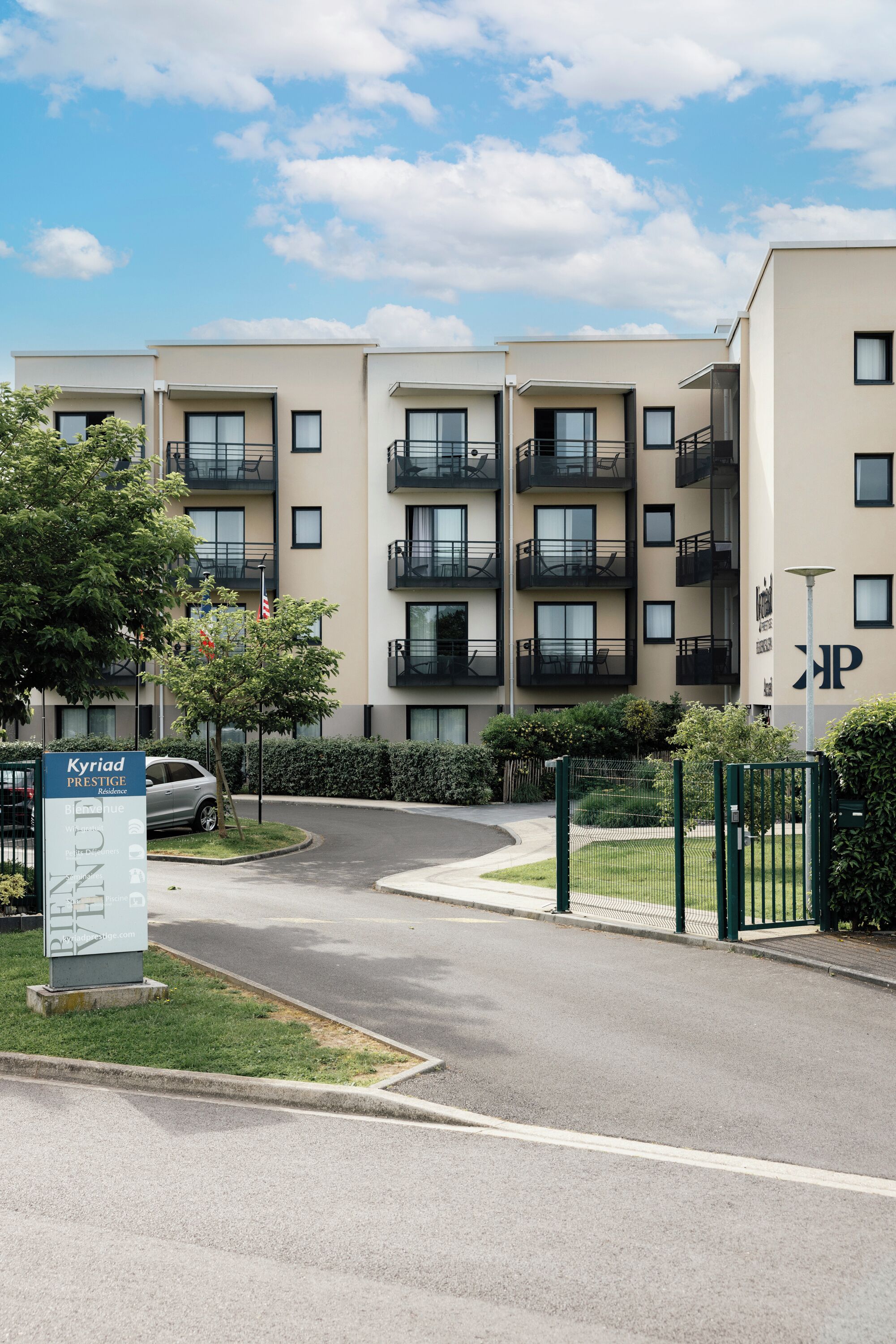 Un edificio residencial de varios pisos con balcones, un área de estacionamiento y un letrero que indica 'Kyriad Prestige Residences'.