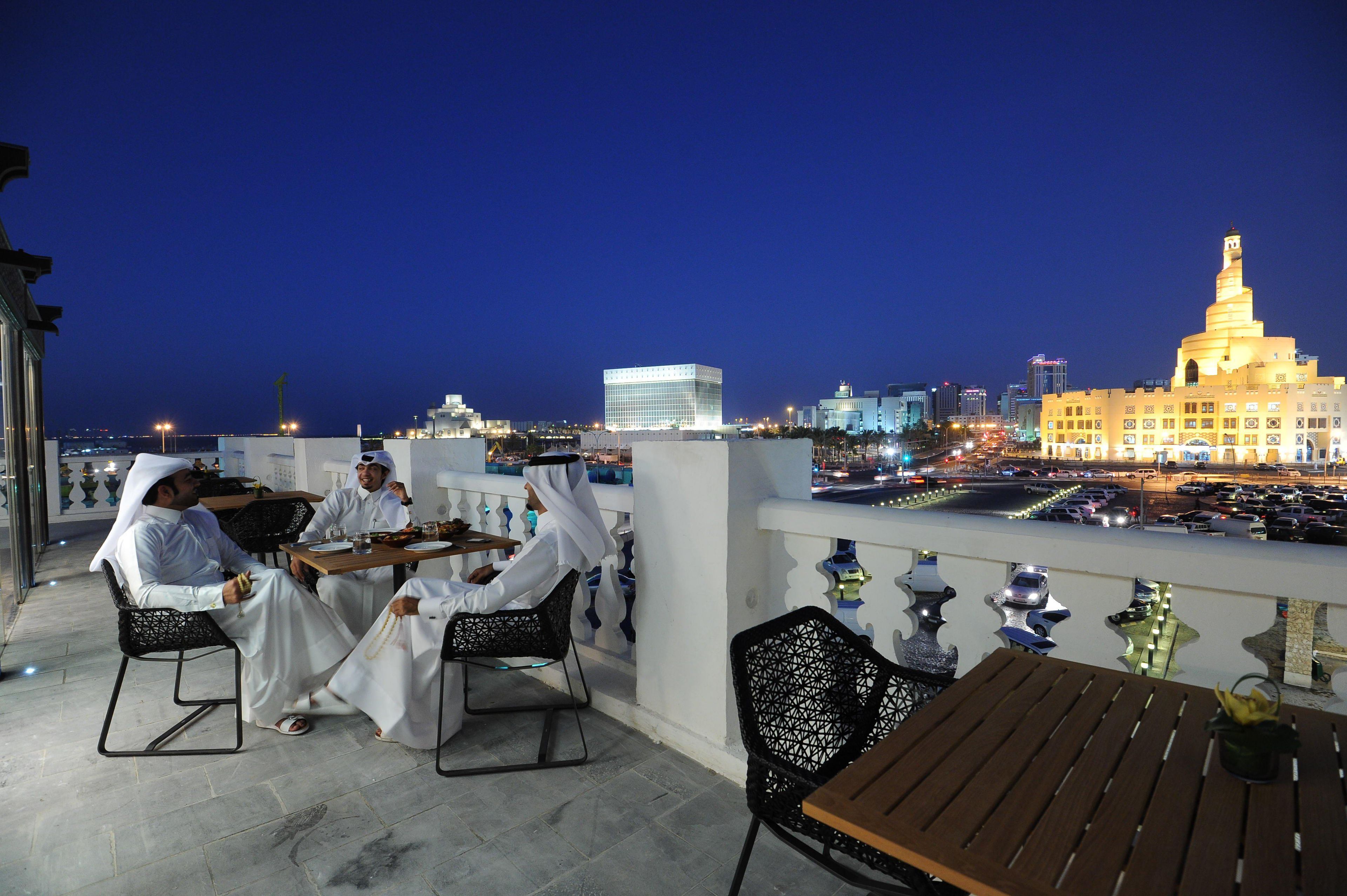 A rooftop dining area with outdoor seating and a cityscape view at night.