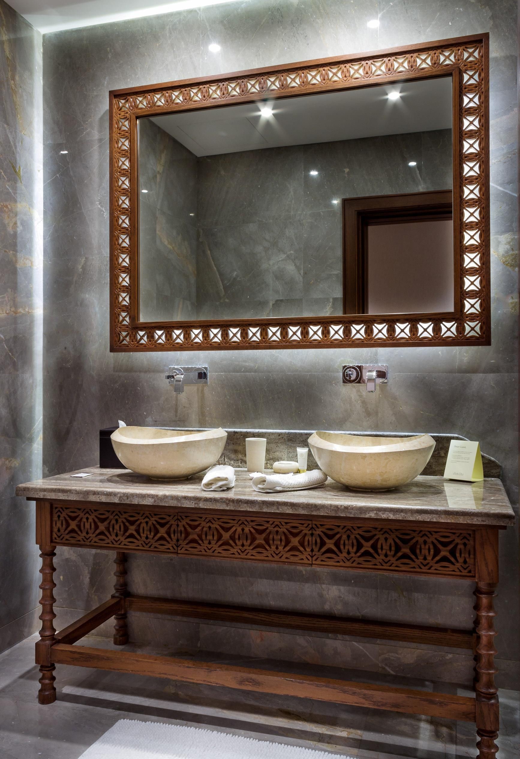 A bathroom with a marble wall, a wooden vanity with two sinks, and a large mirror with a decorative frame.