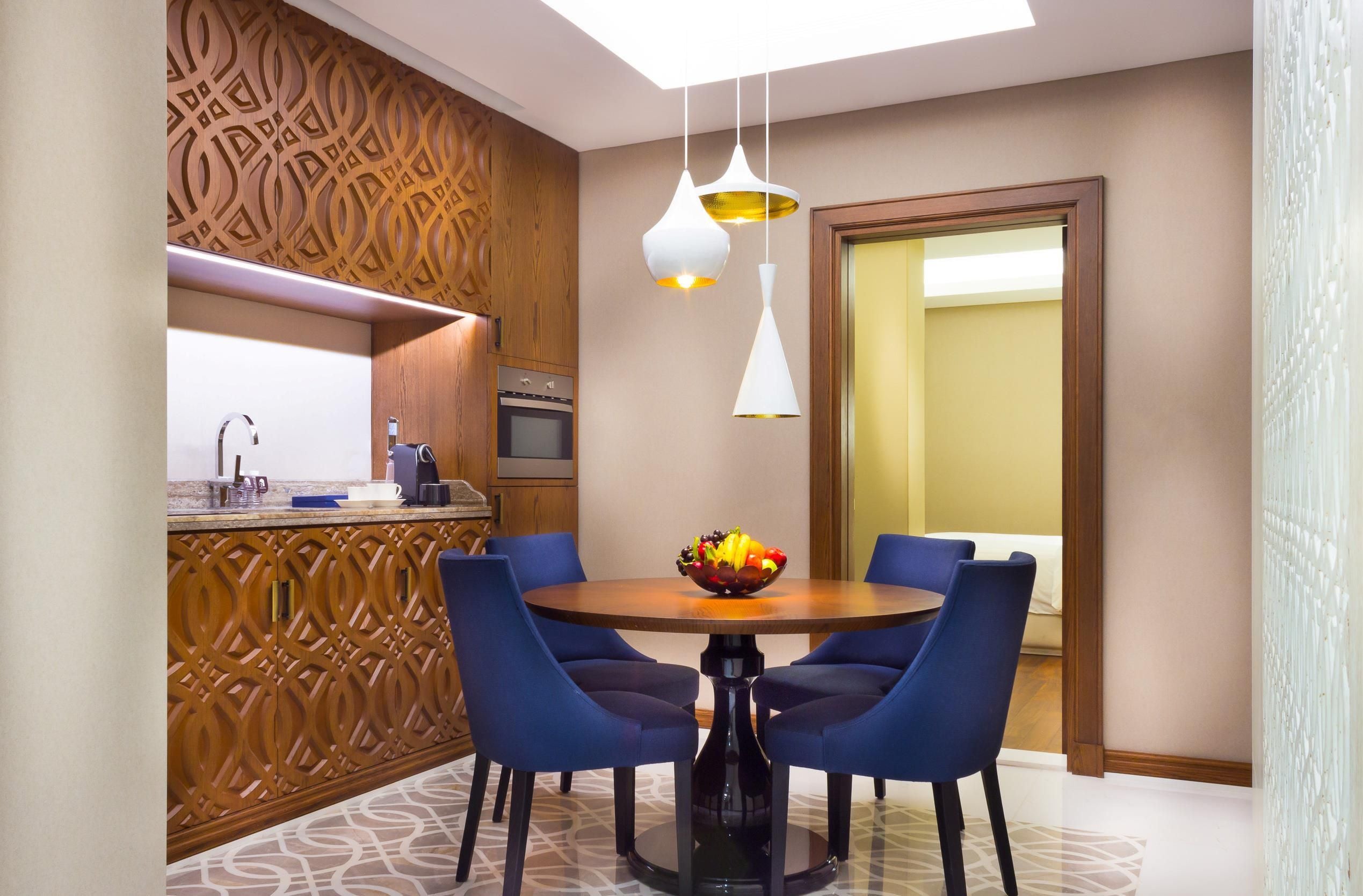 A modern dining area with a round table, blue chairs, and a fruit bowl.
