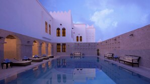 A pool area with lounge chairs and a bench, surrounded by a building with arched windows and a tiled floor. - Souq Waqif Boutique Hotels by Tivoli (Doha)
