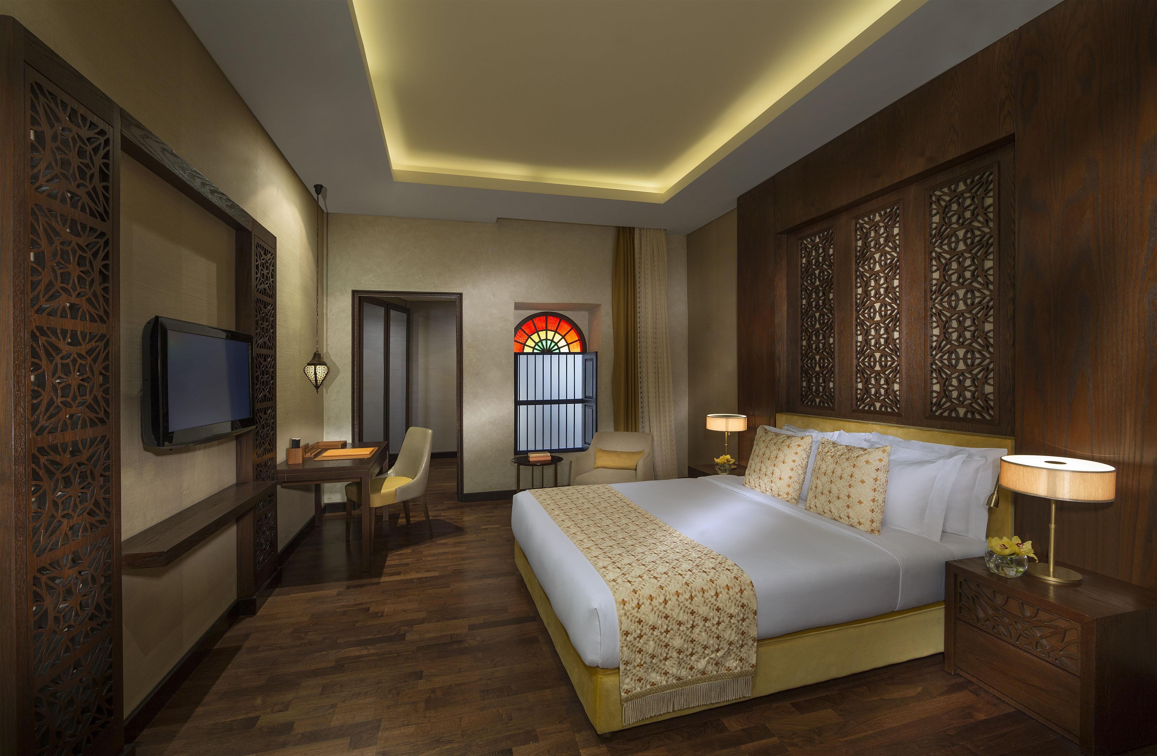 A hotel room with a bed, bedside tables, a TV, a desk, and a chair.