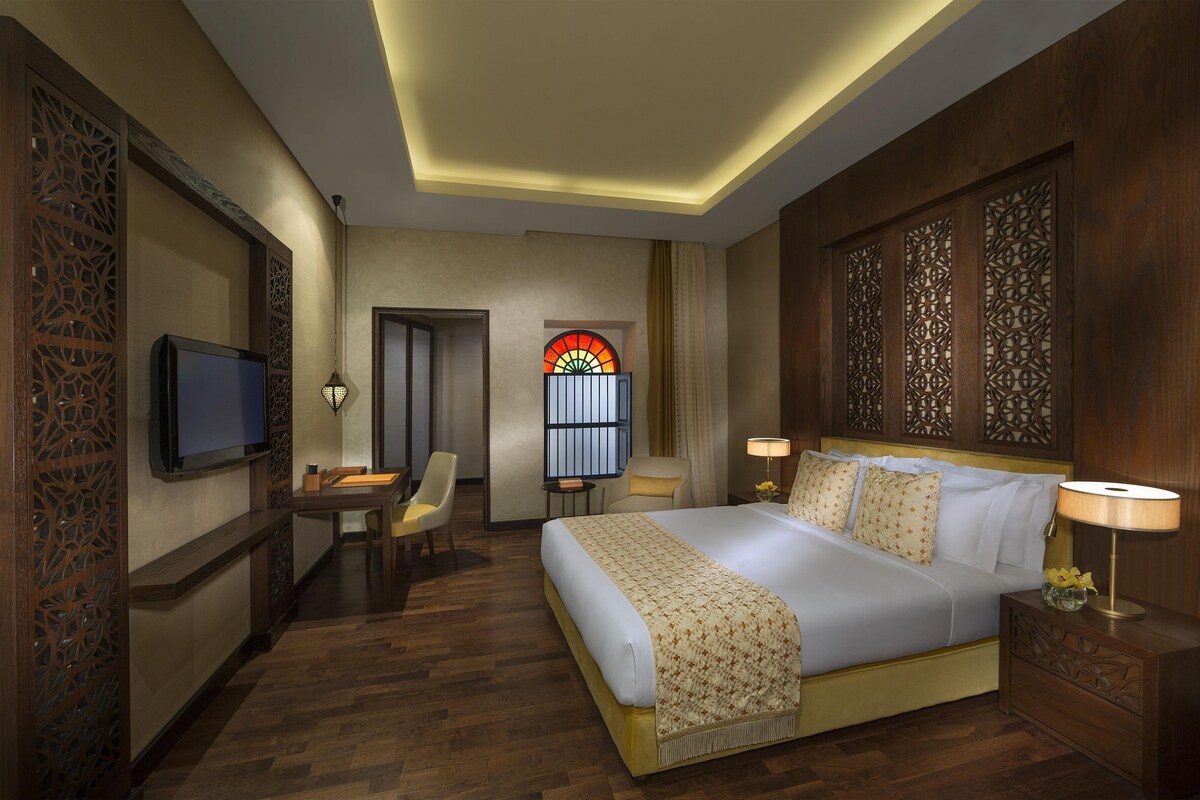 A hotel room with a bed, bedside tables, a TV, a desk, and a chair.