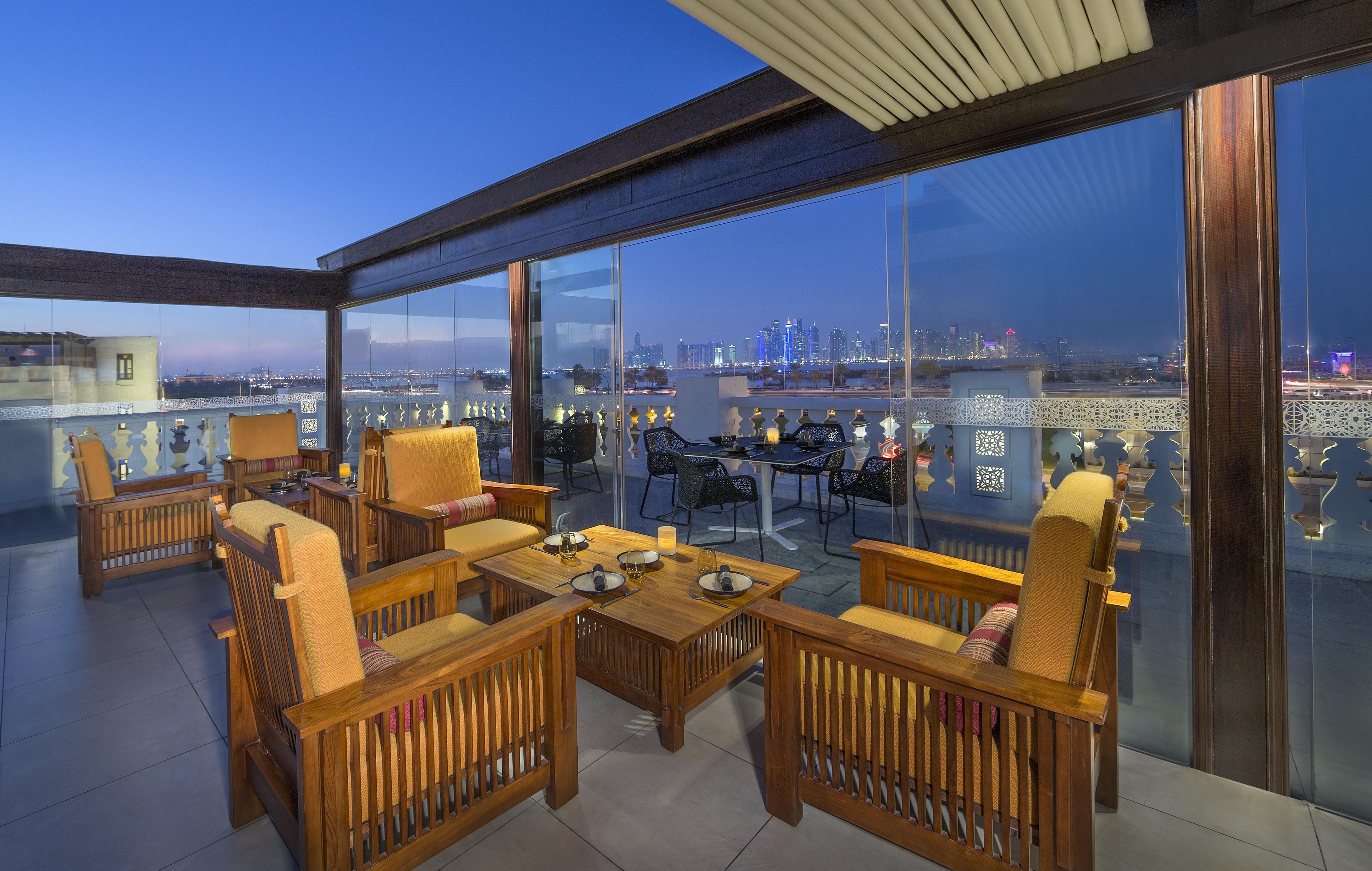 A rooftop terrace with wooden furniture, a dining table, and a city view.