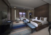 A modern hotel room with a large bed, two seating areas, a TV, and a view of a cityscape.