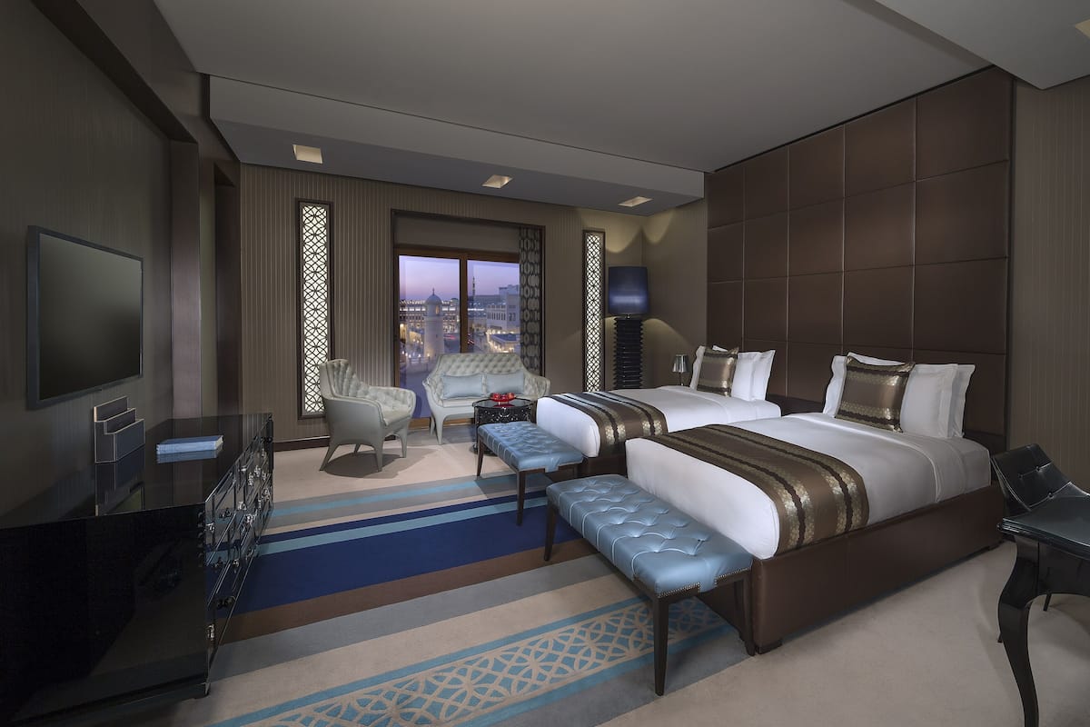 Une chambre d’hôtel moderne dotée d’un grand lit, de deux coins salon, d’une télévision et offrant une vue sur le paysage urbain.