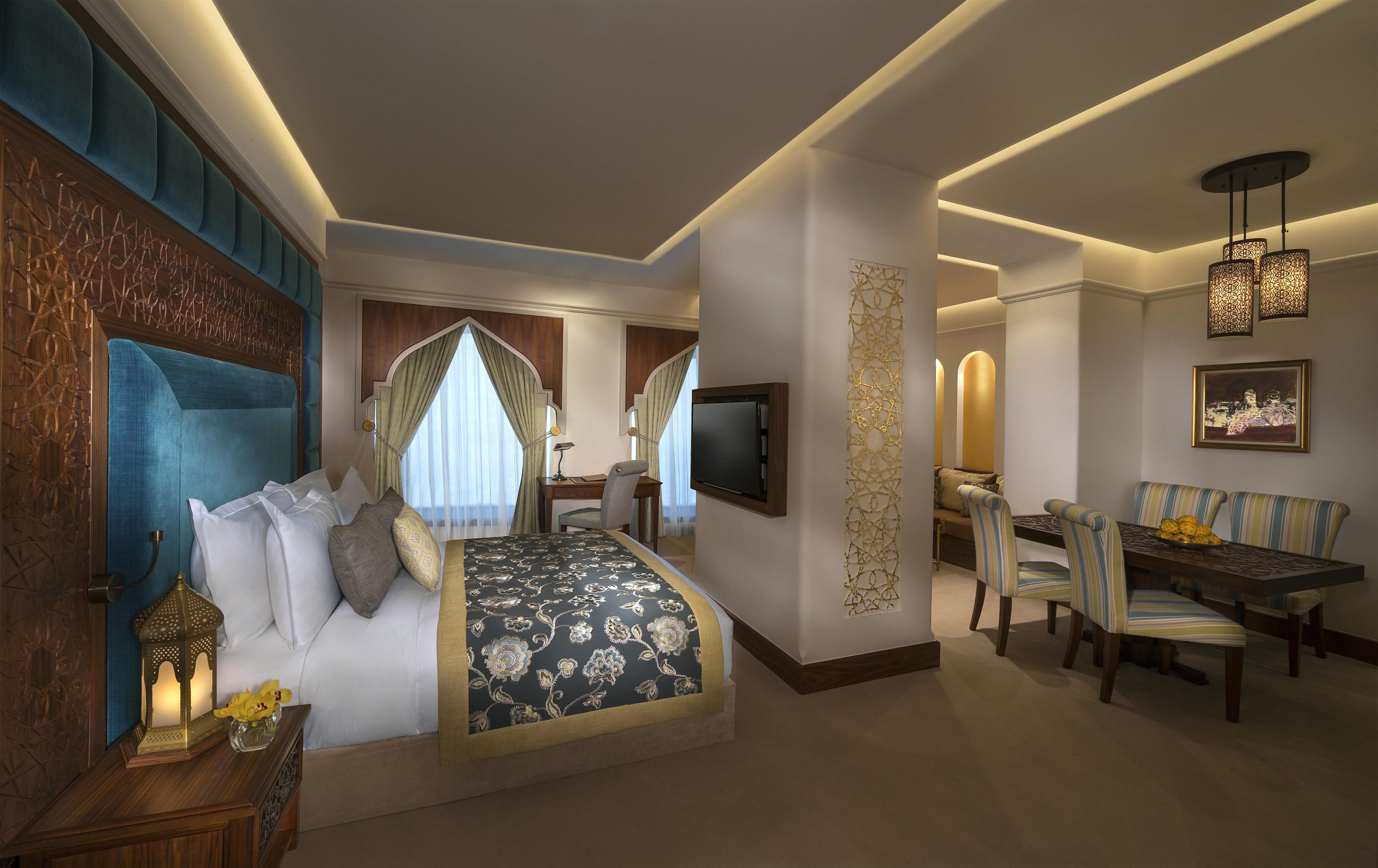 A hotel room with a bed, a desk, a dining area, and a TV.