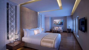 A modern hotel room with a large bed, a nightstand with a lamp, a small table with a vase, and a painting on the wall. - Souq Waqif Boutique Hotels by Tivoli (Doha)