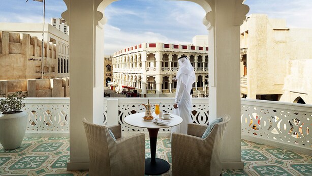 A balcony with wicker chairs, a table with a pitcher, a glass of orange juice, and a cup of coffee. - Souq Waqif Boutique Hotels by Tivoli (Doha)
