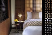 A bedroom with a bed, a bedside table with a vase of flowers, a hanging light fixture, and a wooden headboard.