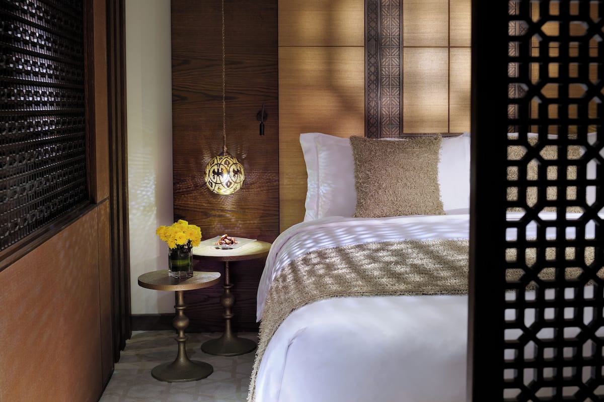 Une chambre à coucher avec un lit, une table de chevet ornée d’un vase de fleurs, un luminaire suspendu et une tête de lit en bois.