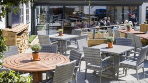 An outdoor patio with wicker furniture, potted plants, and a wooden table. - Old Cock Inn (Harpenden)