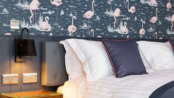 A hotel room with a bed, a nightstand, a lamp, and a wall with a flamingo pattern.