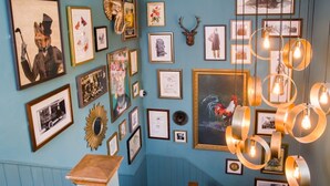 A staircase with a wooden handrail, flanked by blue walls adorned with framed artwork, photographs, and a large painting. - Old Cock Inn (Harpenden)