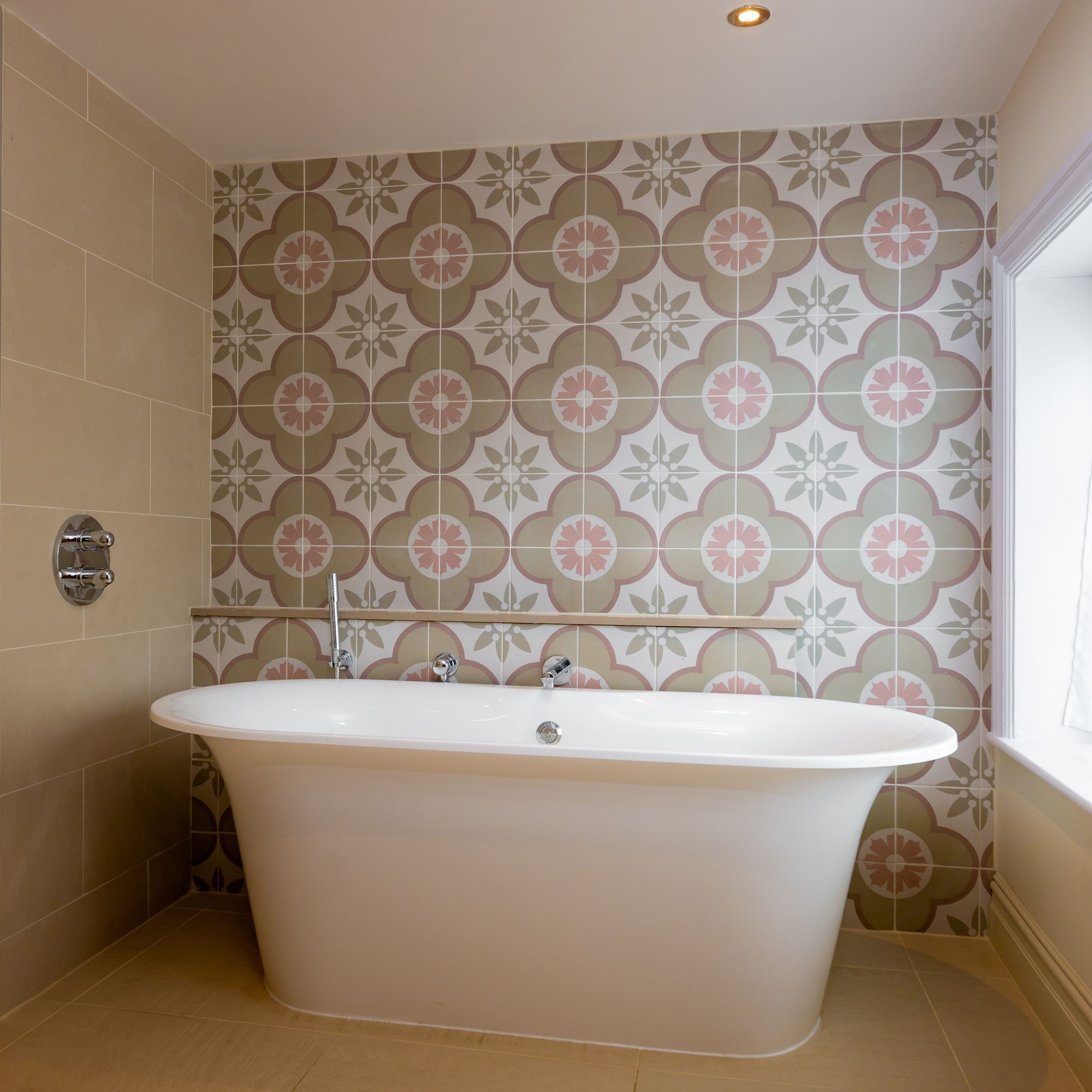 Un baño con una bañera independiente, paredes de azulejos y una ventana.