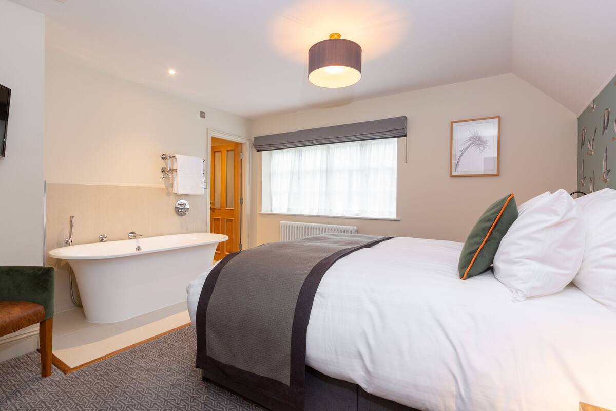 A bedroom with a large bed, a bathtub, and a window with curtains.
