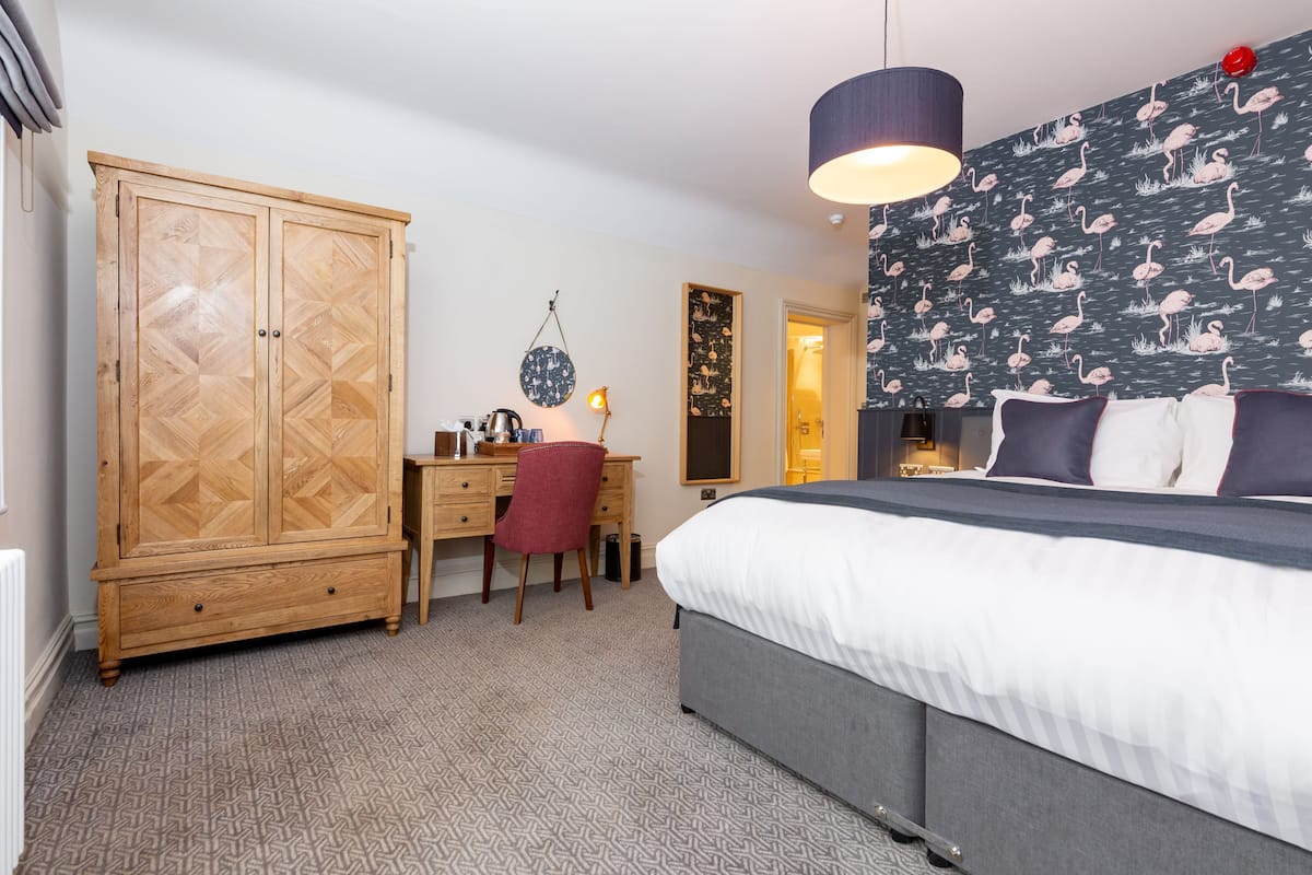 A bedroom with a bed, a desk, a wardrobe, and a patterned wall.