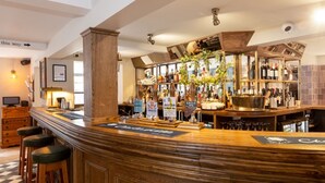 A bar area with wooden bar stools, a variety of bottles, and a sign indicating 'Classic' and 'Jazz Club' beers. - Old Cock Inn (Harpenden)
