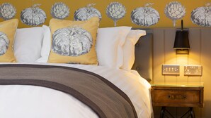 A neatly made bed with white and yellow pillows, a brown throw blanket, and a wooden nightstand with a lamp. - Old Cock Inn (Harpenden)