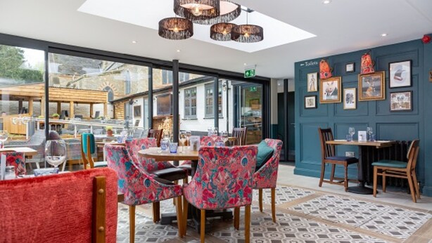 A restaurant with a modern interior, featuring patterned chairs, a patterned floor, and a wall with framed pictures. - Old Cock Inn (Harpenden)
