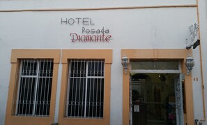 Un hotel llamado "HOTEL Posada Diamante" con dos ventanas de metal y una puerta con un letrero que indica que es un baño público.