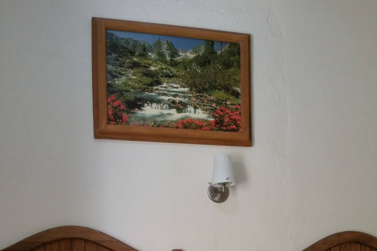A bedroom with two wooden beds, a painting of a landscape, and a wall-mounted lamp.