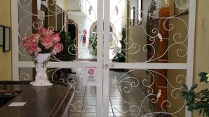 A reception area with a white decorative gate, a wooden reception desk, and a vase of pink flowers. - Hotel Posada Diamante (Querétaro)