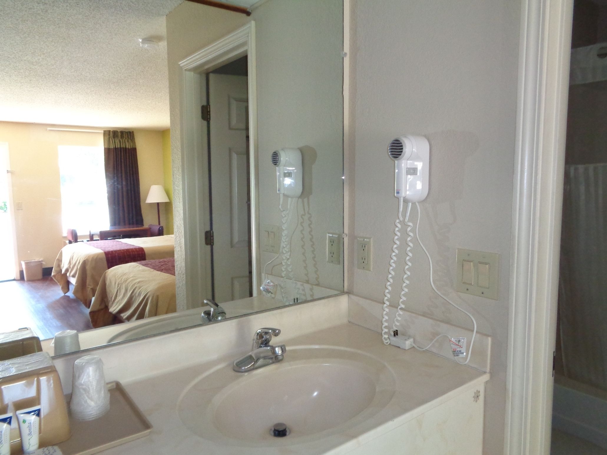 A hotel bathroom with a sink, mirror, and hairdryer on the wall.