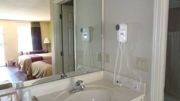 A hotel bathroom with a sink, mirror, and hairdryer on the wall.