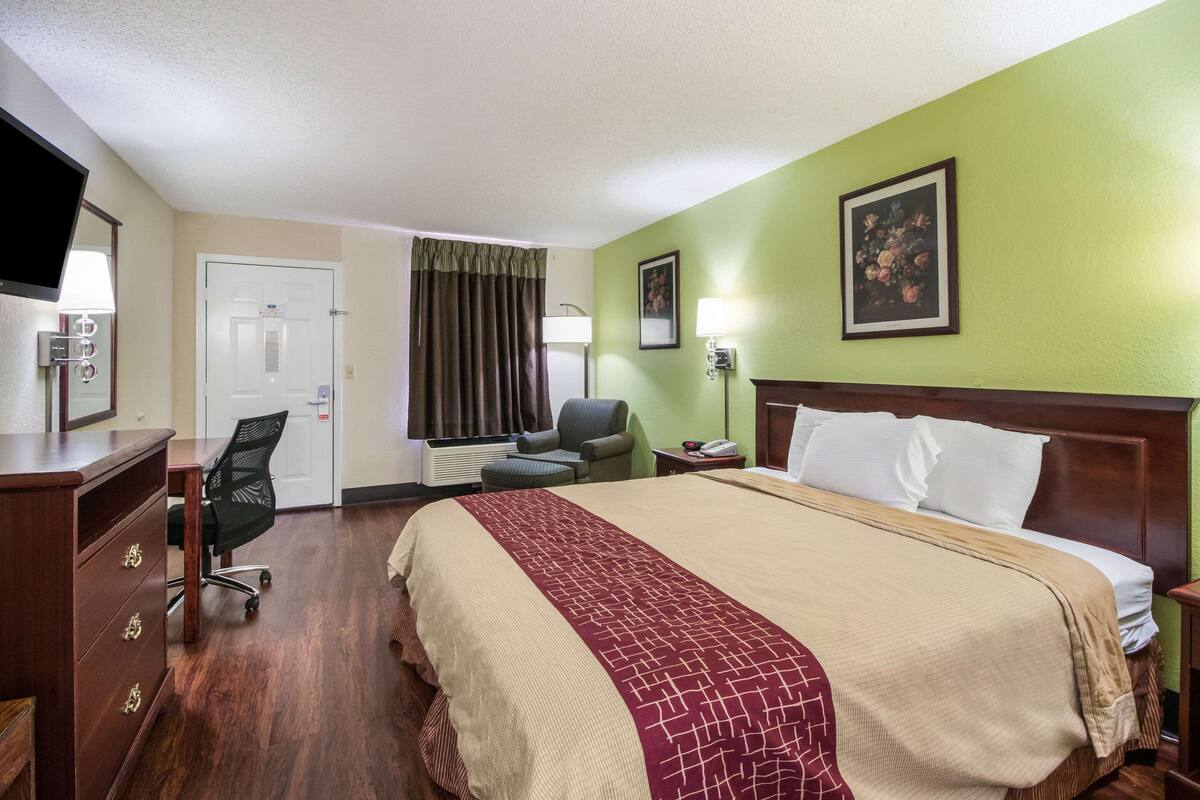 Quarto de hotel com cama, escrivaninha, cadeira e televisão.