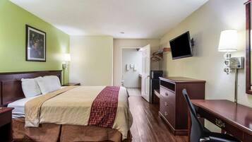 A hotel room with a bed, a desk, a chair, a TV, and a lamp.