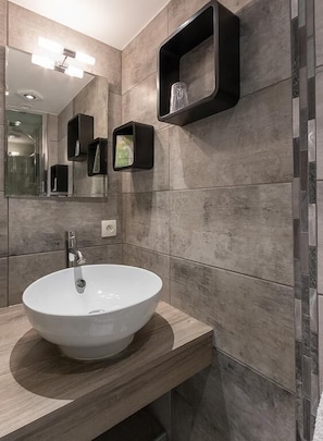 A modern bathroom with a large white sink, a mirror, and built-in shelves. - Hotel du Midi (Thones)