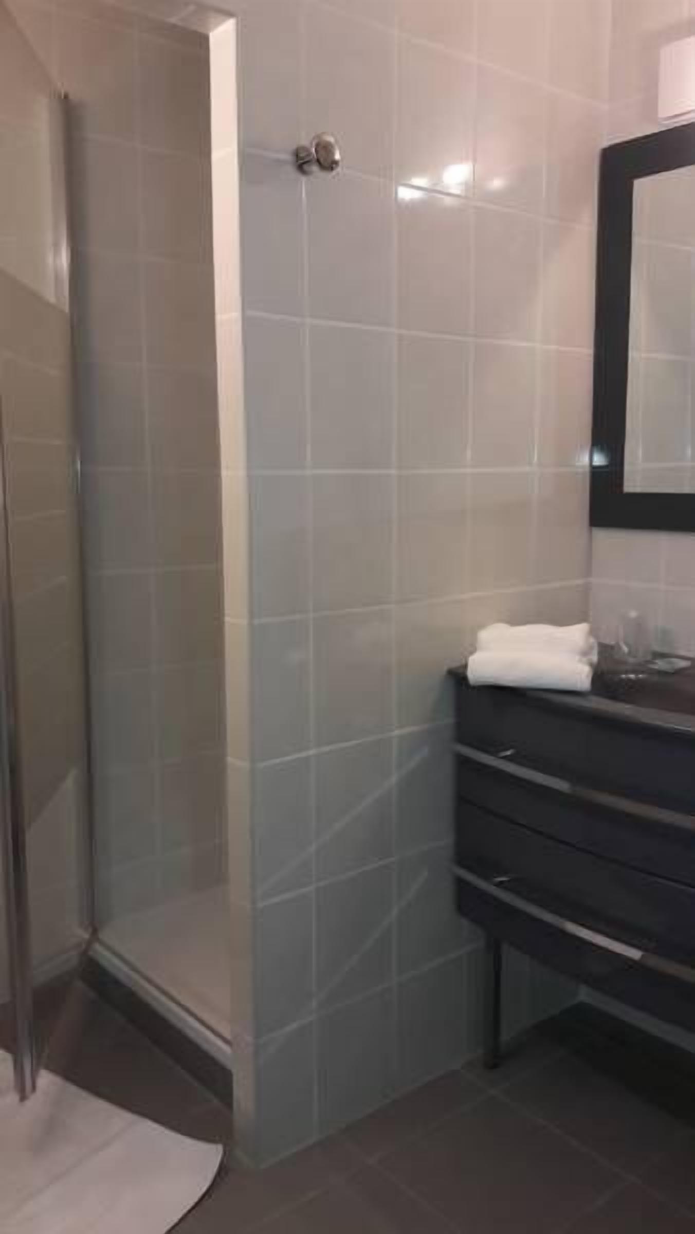Un baño con cabina de ducha de vidrio, tocador oscuro con espejo y baldosas de colores claros.