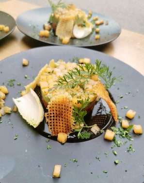 A dish with a crispy texture, garnished with herbs and small cubes, served on a dark plate. - Hotel du Midi (Thones)