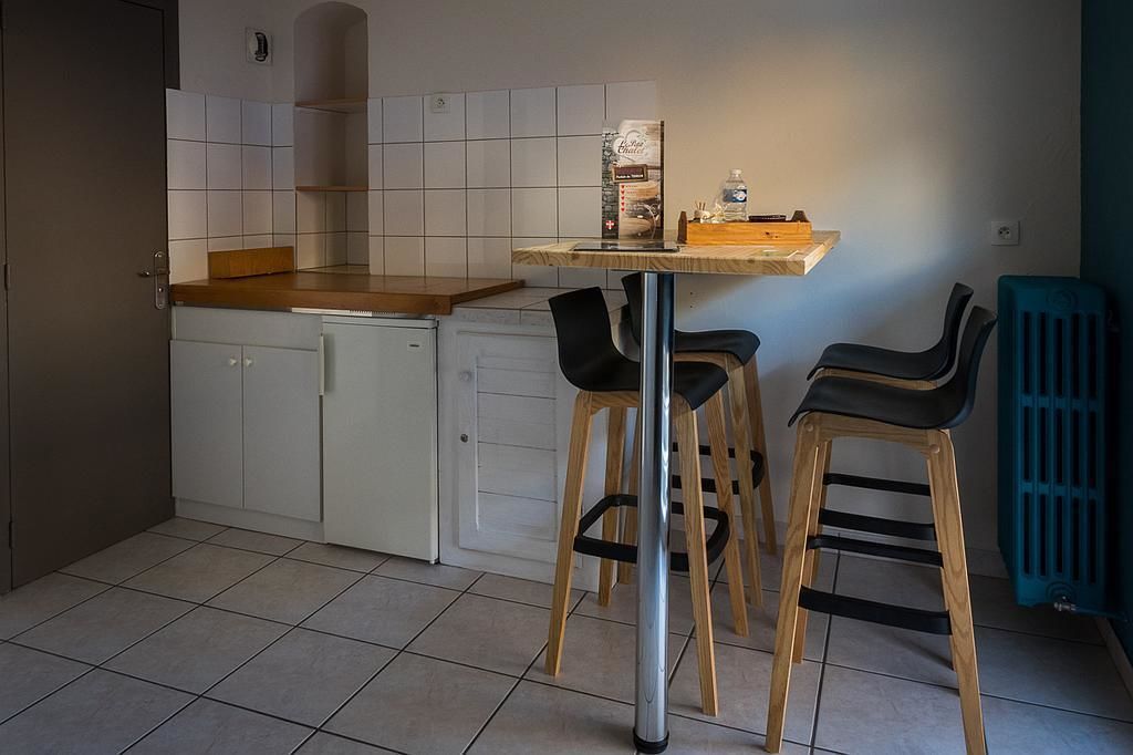 A compact kitchen with white cabinets, a wooden countertop, and two black chairs.