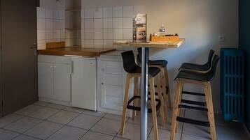 A compact kitchen with white cabinets, a wooden countertop, and two black chairs.