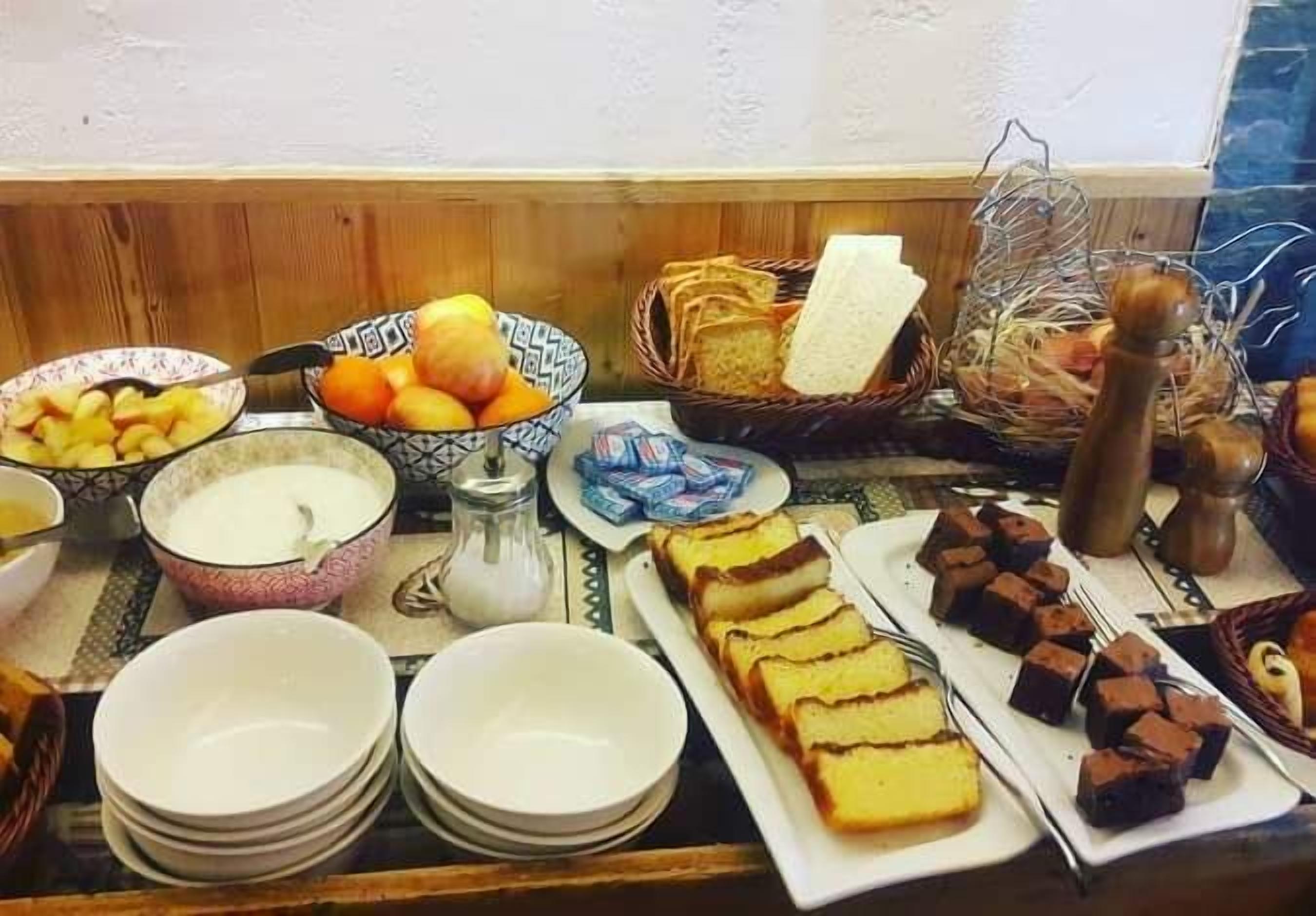 Una mesa de buffet con diversas opciones de comida, incluyendo frutas, pan y postres.
