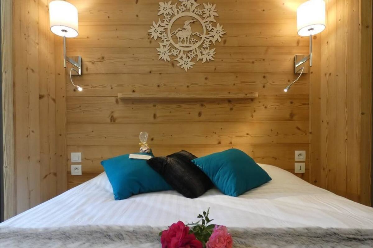 Habitación con paneles de madera, una cama, dos luces fijadas a la pared, un adorno mural y un pequeño estante.