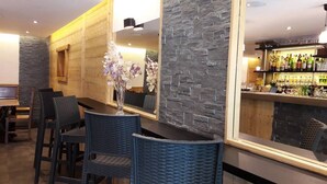 A bar area with wicker chairs, a vase with flowers, and a stone wall. - Hotel du Midi (Thones)
