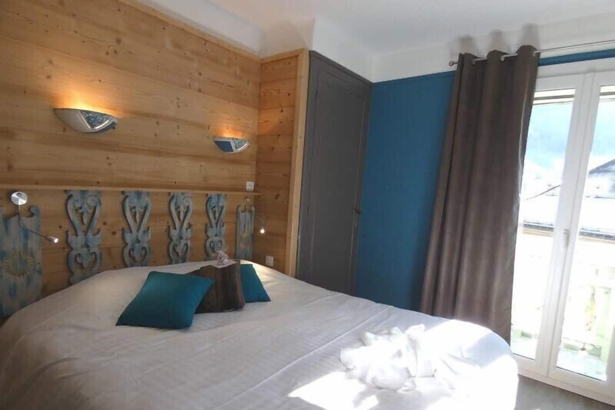 Un dormitorio con cabecera de madera, cama con ropa de cama blanca y vistas al exterior a través de una puerta corrediza.