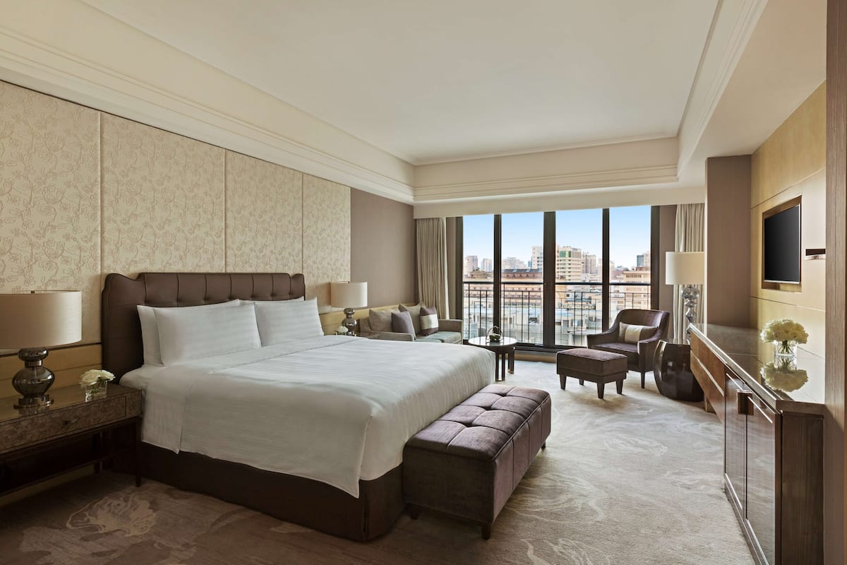 Ein geräumiges Hotelzimmer mit einem großen Bett, einer Sitzecke, einem Fernseher und Blick auf die Stadt.
