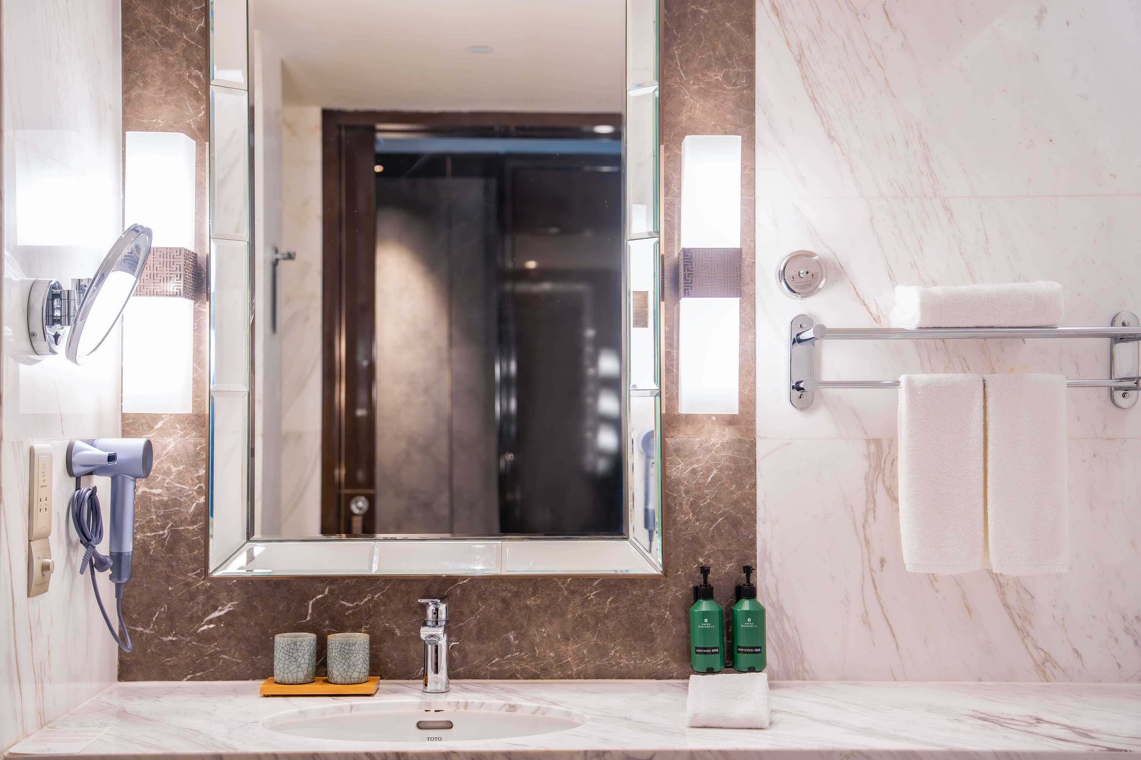 A bathroom with a marble sink, a large mirror, a towel rack, and two green bottles of shampoo.