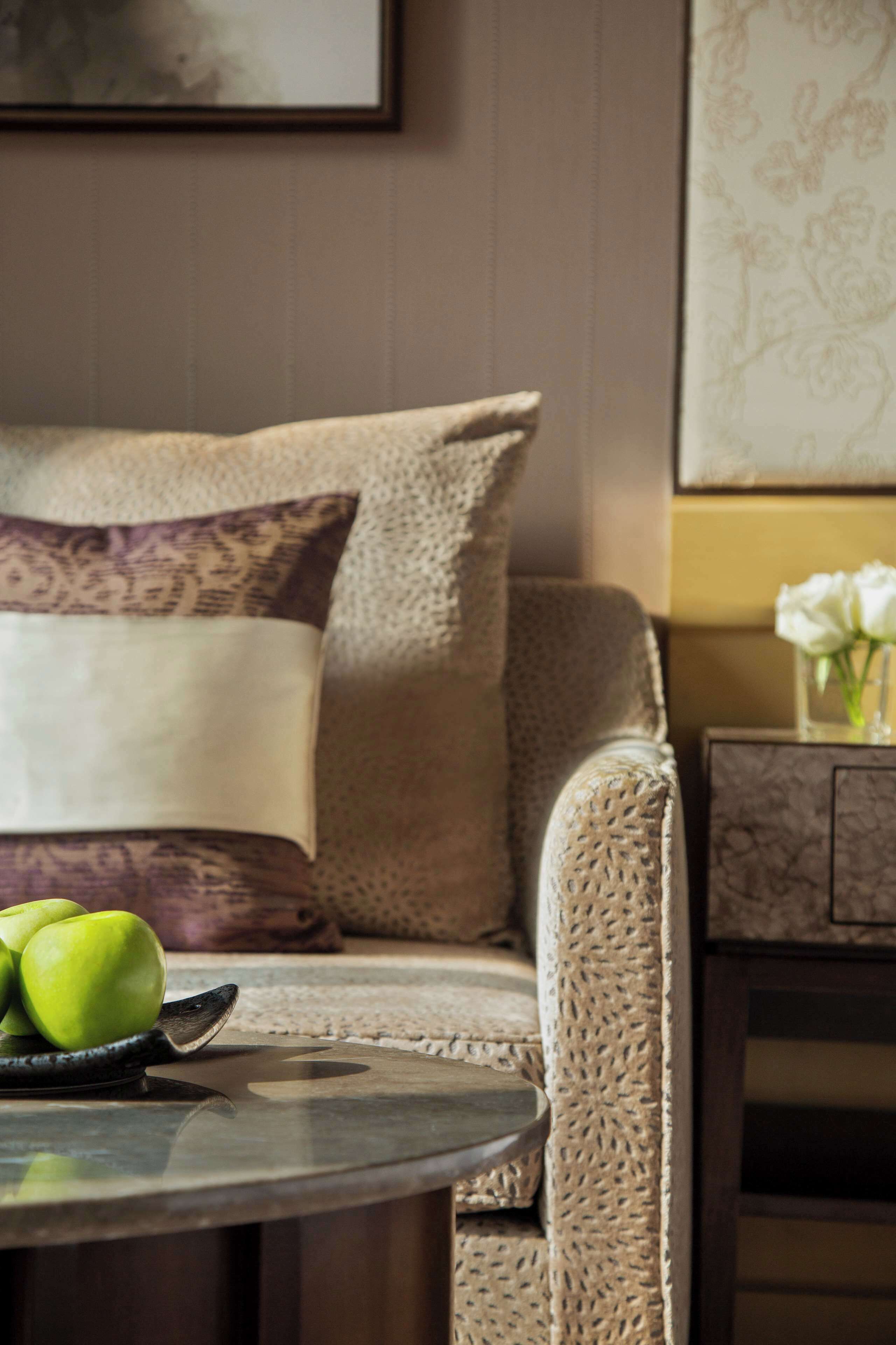 A room with a sofa, a small table with apples, and a vase with flowers.