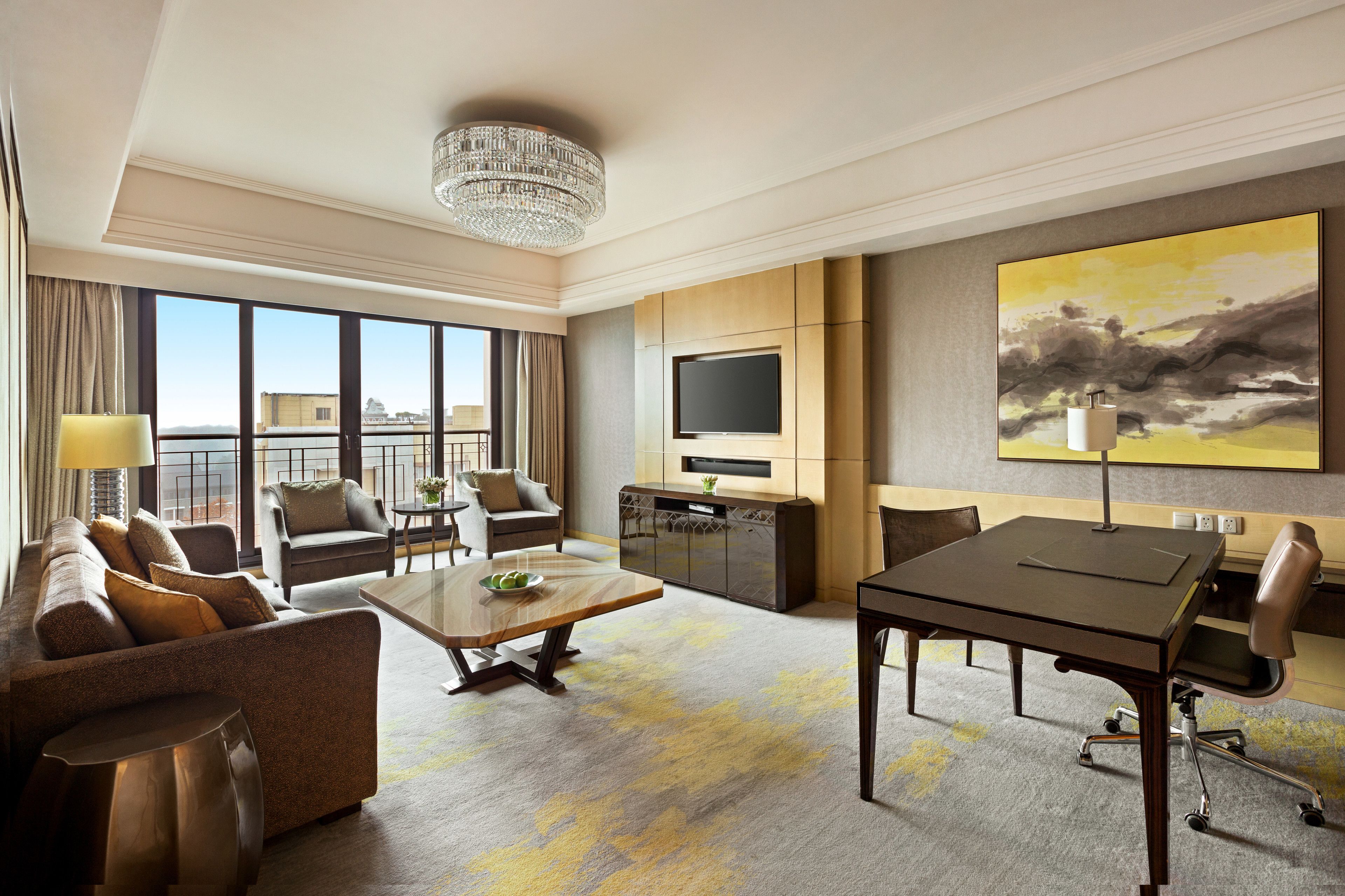 A modern hotel room with a sofa, armchairs, a dining table, a TV, and a large painting.