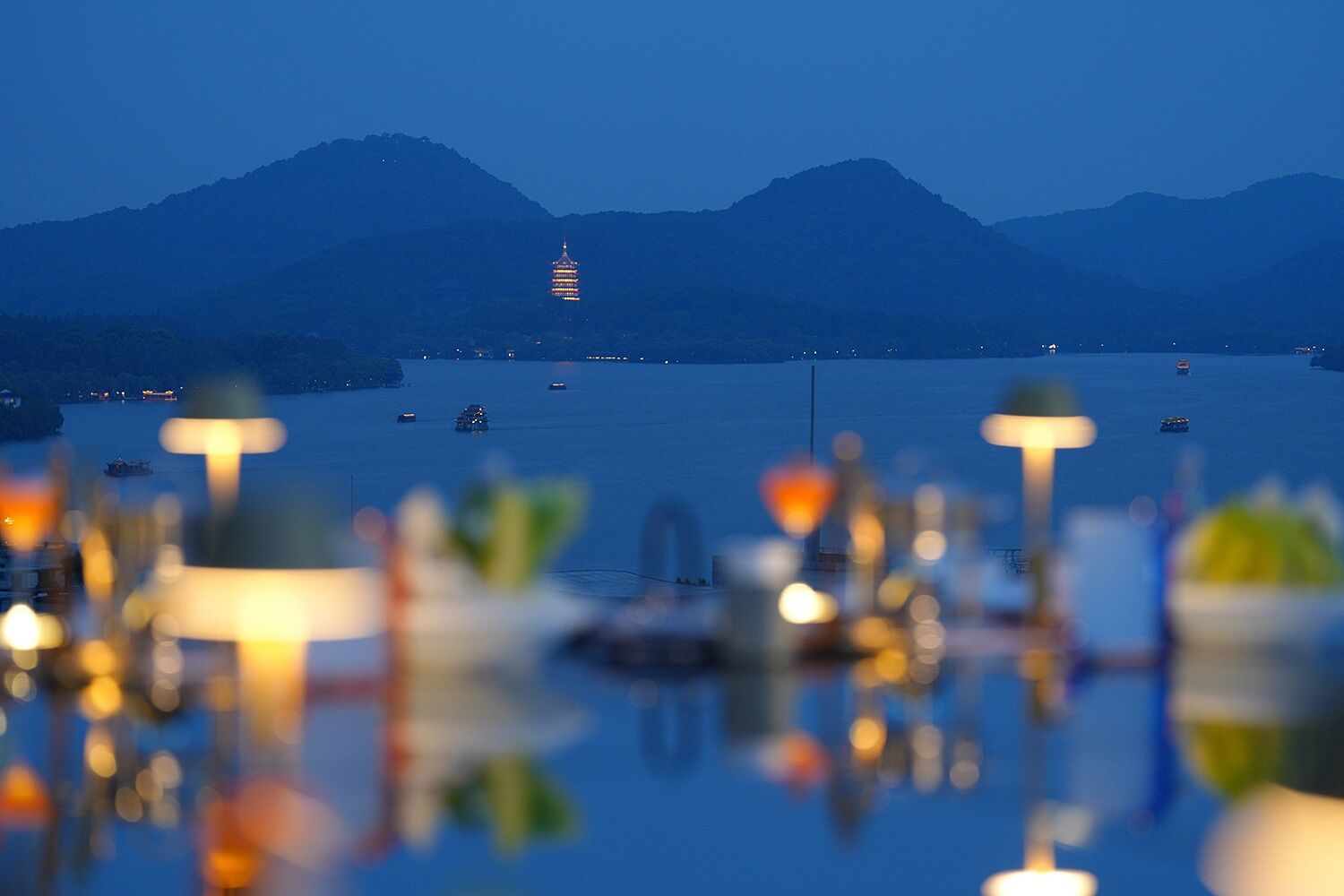 A view of a body of water with mountains in the background and a lit building in the distance.
