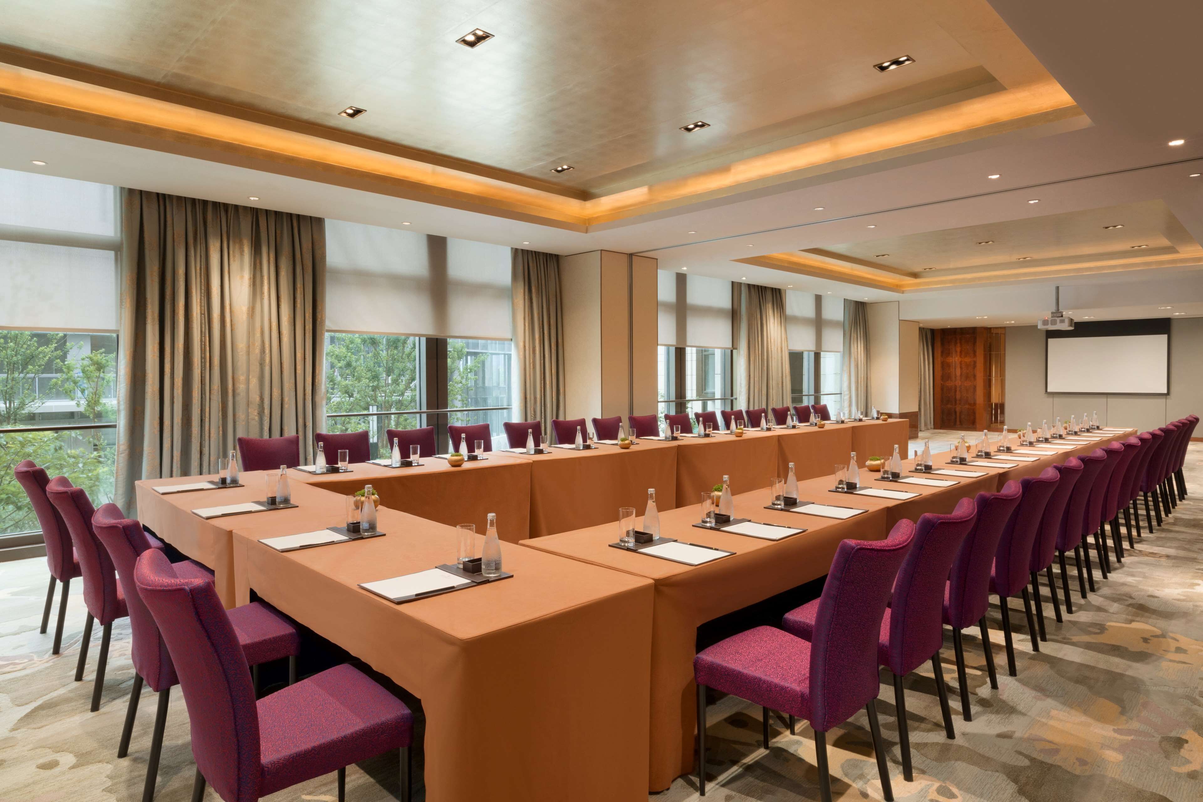 A conference room with a long table, purple chairs, and a projector screen.