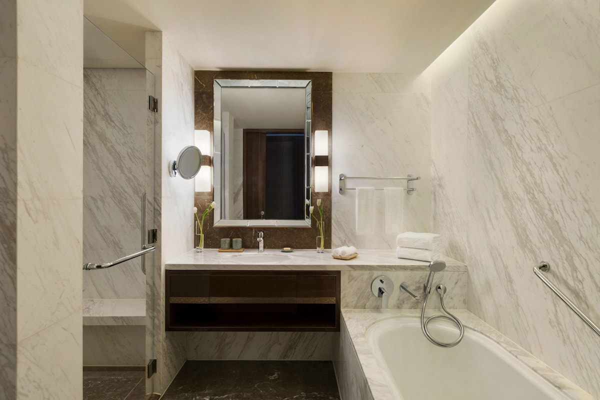 A bathroom with a marble vanity, a bathtub, a shower, and a large mirror.