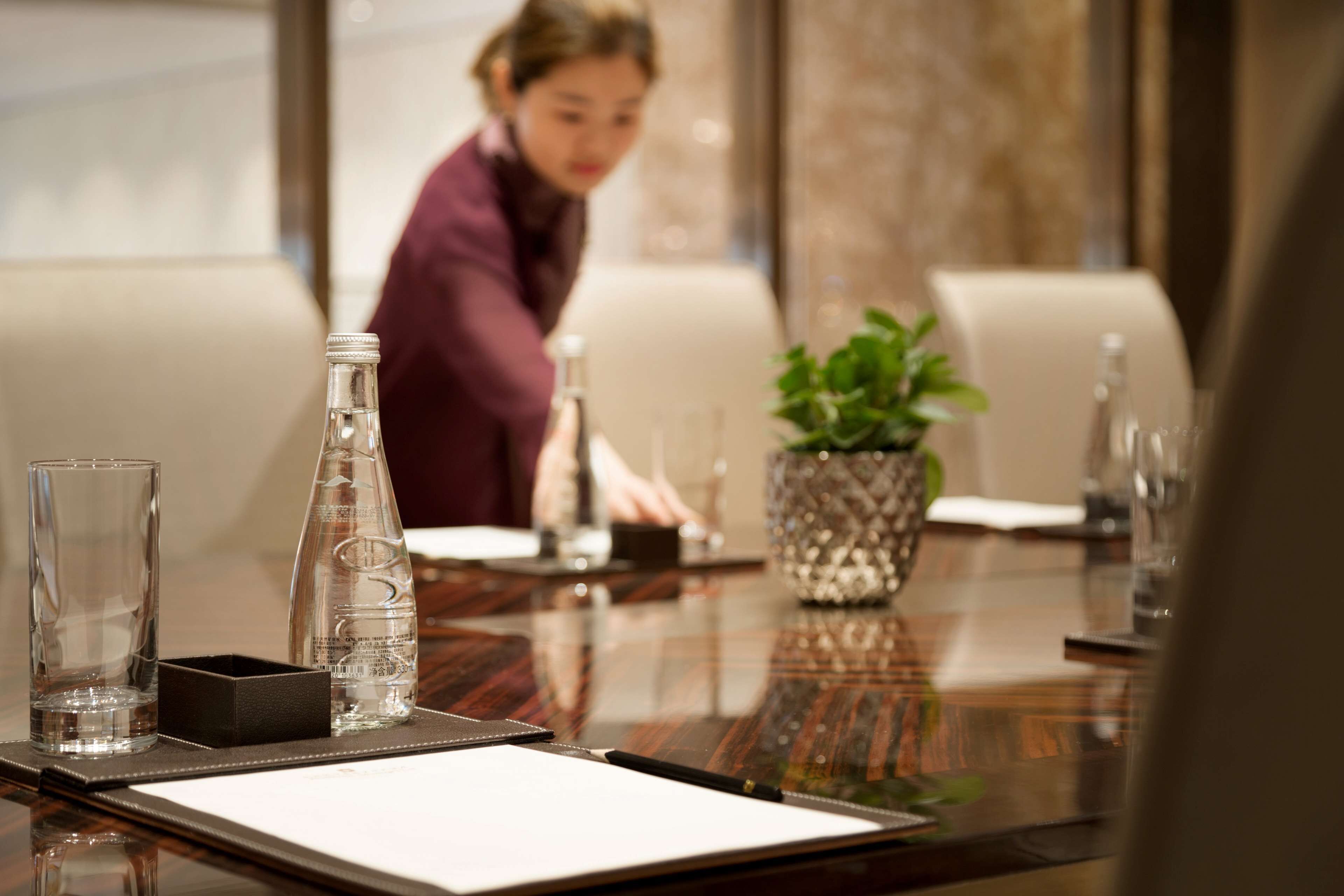 A conference table with a bottle, glasses, and a plant.