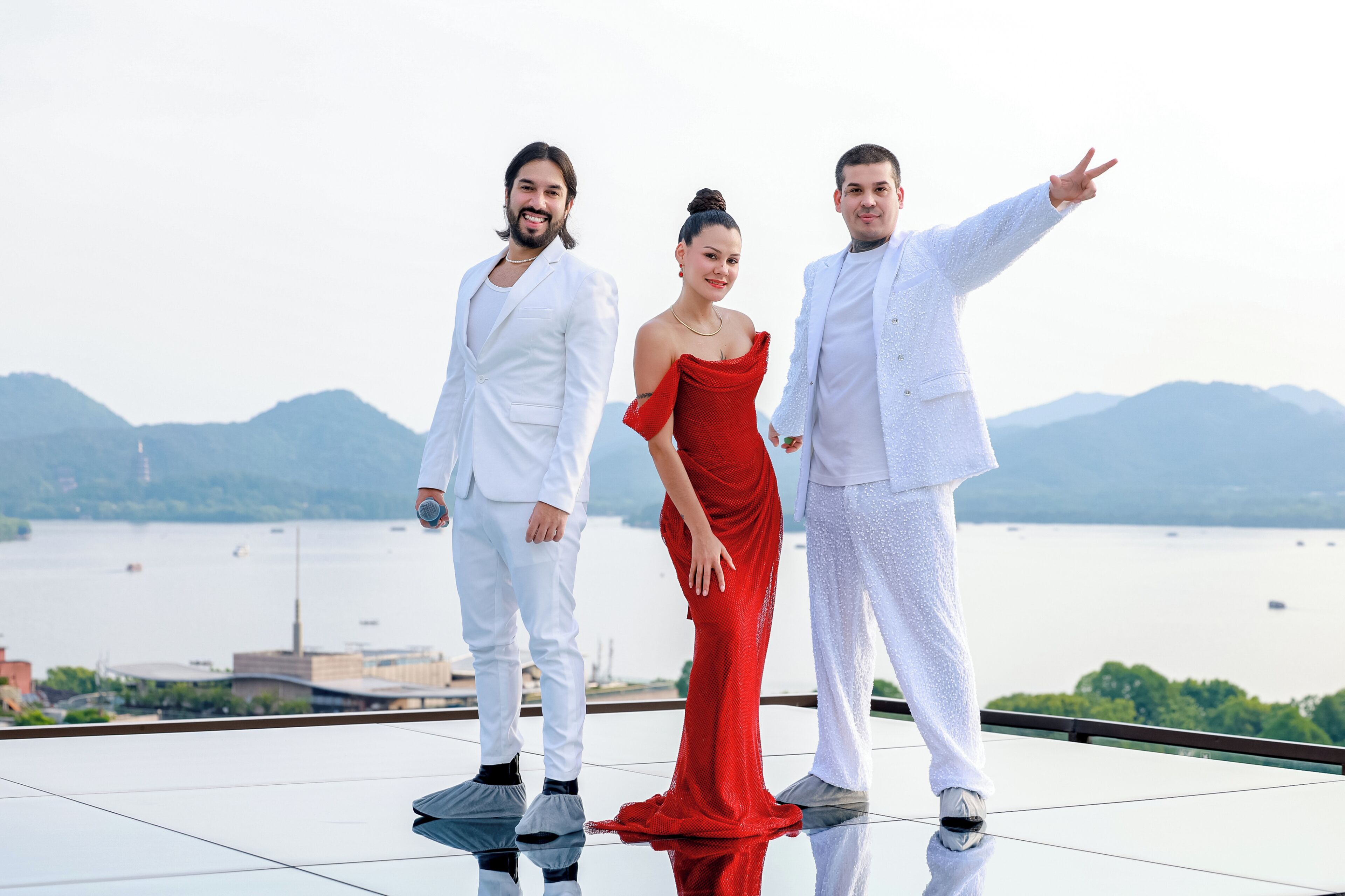 Three people standing on a reflective surface with a body of water and mountains in the background.